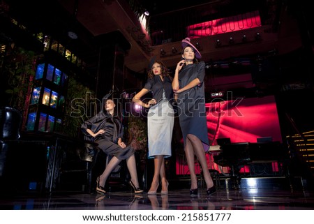 Three beautiful models in a stylish designer clothes posing in a nightclub