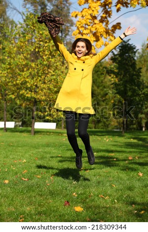 Beautiful woman in yellow coat jumping in autumn park