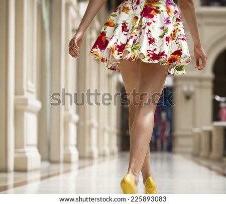 Beautiful shapely female legs back view in flowers dress in the shop