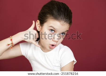 Little Girl making a call me gesture, against background of burgundy wall