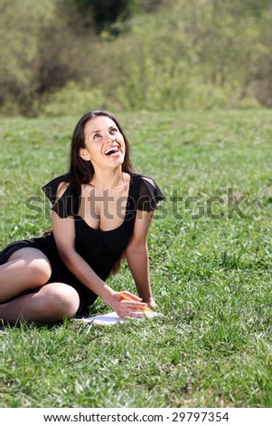 The young beautiful woman lays on a grass in park with a diary in hands
