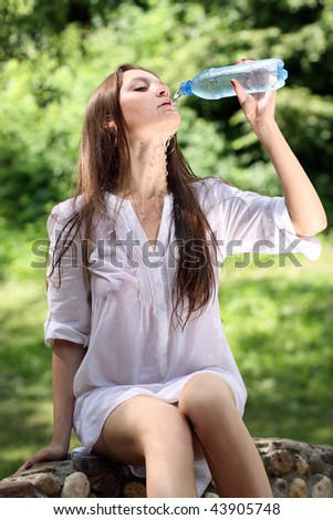 Young beautiful woman drinks mineral water  in park