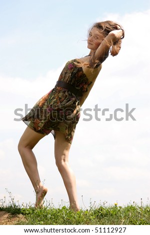 Young woman in summer dress dancing on a background of the blue sky