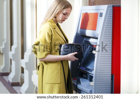 Blonde lady using an automated teller machine . Woman withdrawing money or checking account balance