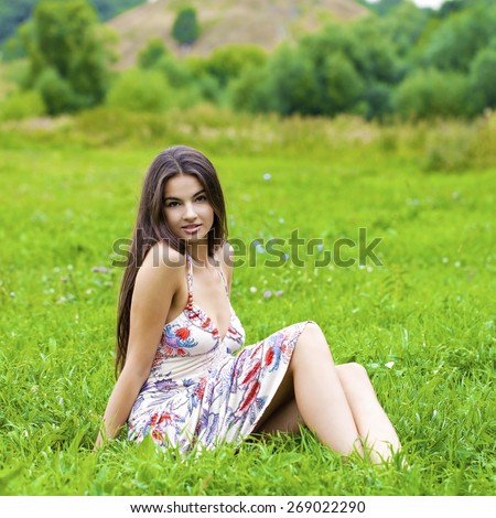 Sexy woman in long dress sitting on green grass