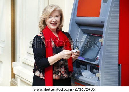 Mature blonde woman with credit card in hand near automated teller machine in shop