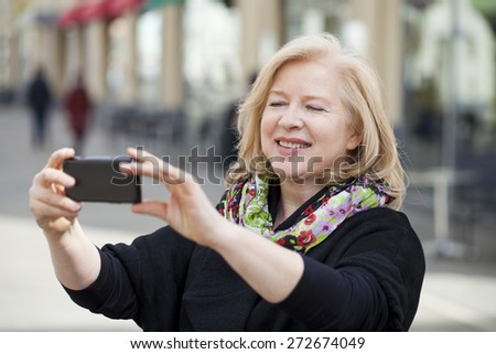 Mature beautiful blonde woman photographed on a cell phone on spring street