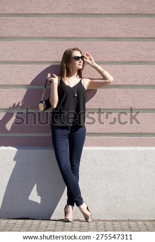 Full length portrait of a beautiful woman in dark blue jeans and black blouse on wall background