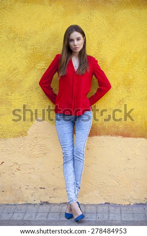 Portrait in full growth the young beautiful girl in blue jeans and a red shirt on the background of color wall