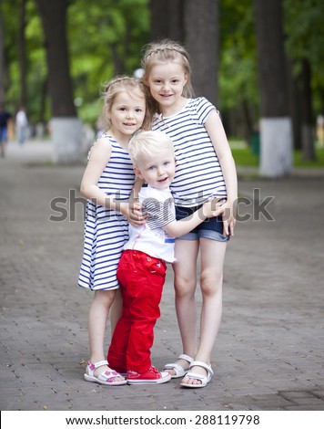 Blonde Little boy and two older cousins sisters, meeting in the summer park