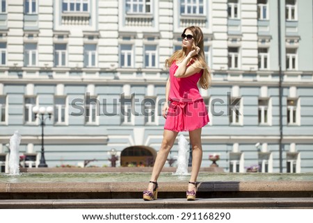 Young beautiful blonde woman in red short dress posing outdoors in sunny weather