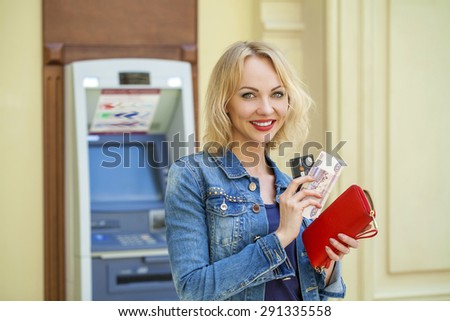 Blonde lady using an automated teller machine. Woman withdrawing money or checking account balance