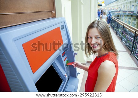 Young happy brunette woman withdrawing money from credit card at ATM