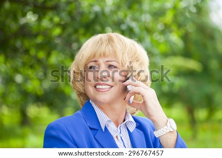 Close up portrait of an elderly beautiful blonde woman talking on a cell phone in a summer park