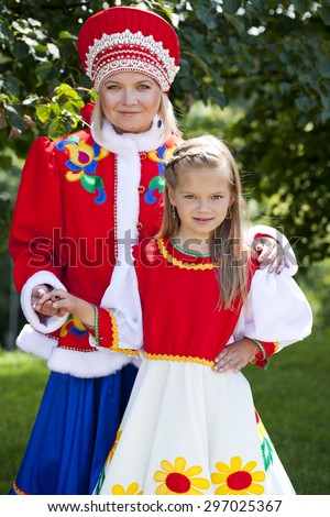 Portrait of mother and daughter in a national Russian costume on a background of green summer park
