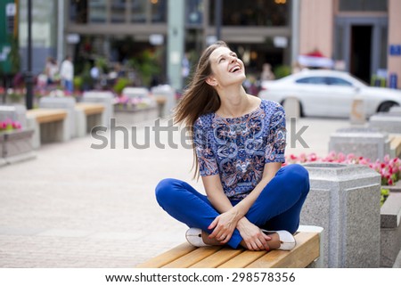 Happy Beautiful young woman sits on a bench in a summer street
