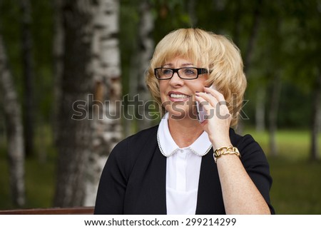 Elderly business woman in jacket sittin on bench with daily log, outdoor summer park