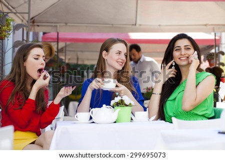 Three young beautiful girls girlfriend drinking tea in a summer cafe