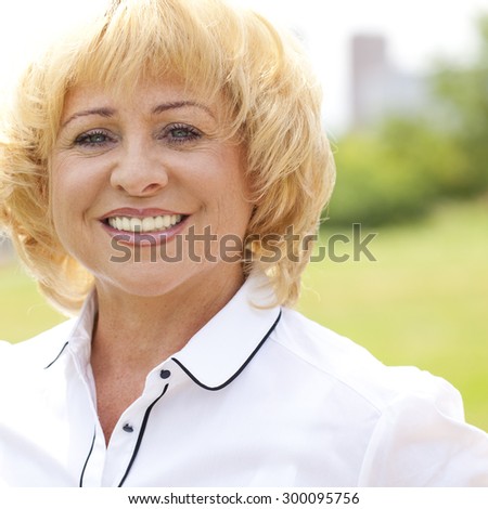 Happy elderly woman in a white jacket on the background of summer park