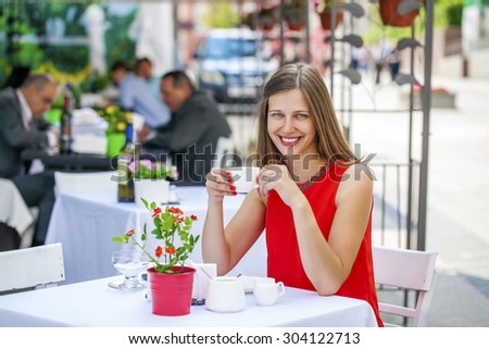 Young happy beautiful brunette girl sitting in a coffee shop on summer street city