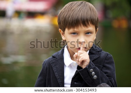 Young beautiful Little Boy has put forefinger to lips as sign of silence