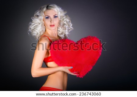Valentine\'s Day.Portrait of a blonde in red lingerie holding a big red heart on a gray background
