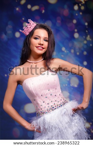 Beautiful cheerful brunette girl in a pink dress and pink crown on his head. mini with sequins and feathers. long hair.bokeh