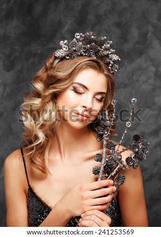 Winter Girl in Luxury fantasy in a wreath of cones on a blue background.Closeup portrait of beautiful snow queen with crown on head.stylish shiny head accessories. fashion for Christmas holidays