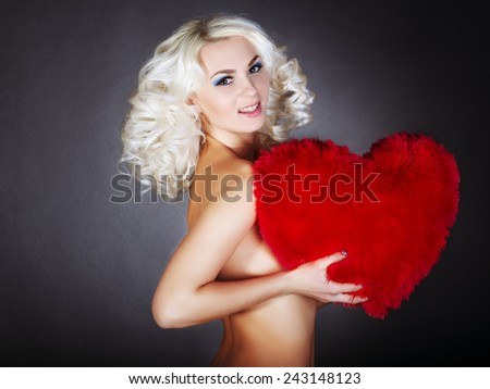 naked girl holding a big red heart in hands. blonde in red lingerie chest covers red heart. on a gray background.Valentine\'s Day