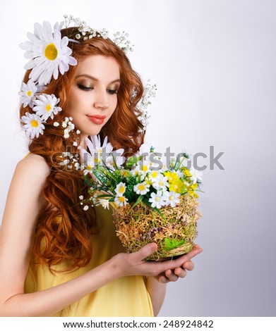 red-haired girl with daisies in her hair holding a bouquet of daisies on a gray background