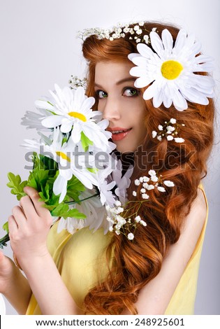 red-haired girl with daisies in her hair smelling a bouquet of daisies. flowers near the girl\'s face