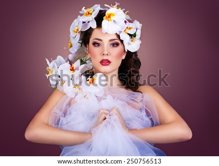 girl with orchids flower in her hair. Professional Make-up.Makeup. Fashion Art.Hairstyle with flowers. Fantasy girl portrait . Bouquet of Beautiful Flowers on lady's head.brunette in a tulle dress
