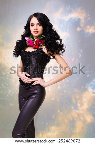 Glamorous woman in black leather corset and a wreath of roses and orchids in the neck. long black curly hair.background rain