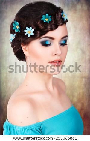 fashion portrait of a girl with a bright turquoise blue make-up and flowers in her hair. clean skin. bright colors . aged background