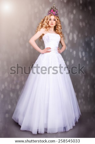The bride in a magnificent white wedding dress on a gray background.beauty portrait of a blonde with perfect makeup and a crown of flowers on her head.curly-haired blonde with flowers in her hair