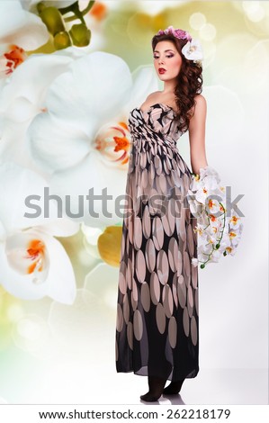 fantasy girl in long dress with flowers in her hair and with a bouquet of orchids in their hands. against the background of orchid flowers