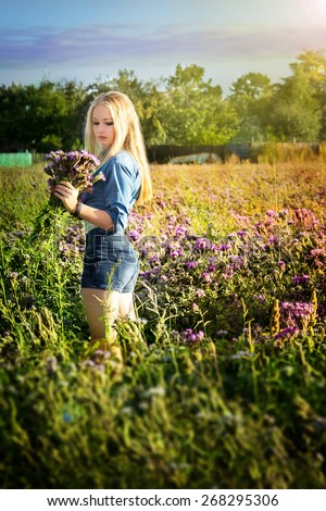 girl with a bouquet of wild flowers in the field.beautiful woman with long curly hair in motion hold in hand a bouquet of wild flowers in grass field