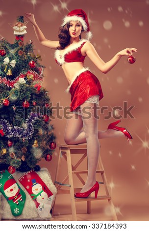 sexy woman dressed as Santa decorates a Christmas tree