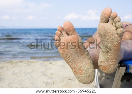 man's feet with sand on a summer beach