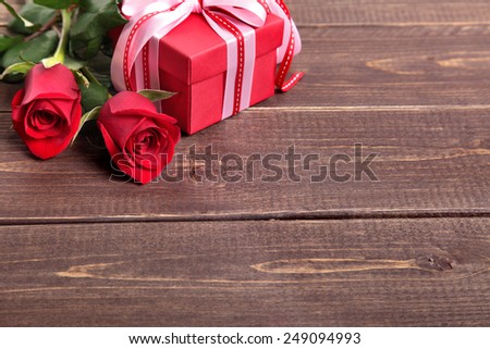 Valentine background of gift box with ribbon and bow and two red roses on wood. Space for copy.
