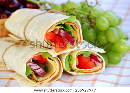 Wrap sandwich : Ham and cheese wrap sandwiches with grapes on table cloth