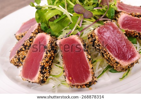 Seared tuna coated sesame seeds with green salad on white plate