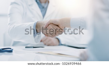 Doctor and patient shaking hands in the office, they are sitting at desk, hands close up