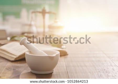 Mortar and pestle with pharmaceutical preparations\'s book and herbs on a wooden pharmacist table, traditional medicine and pharmacy concept