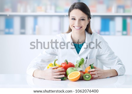 Smiling nutritionist in her office, she is holding healthy vegetables and fruits, healthcare and diet concept