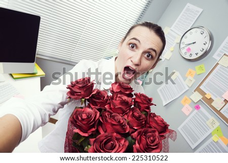 Cheerful female office worker holding red roses bouquet and looking at camera.