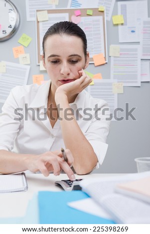 Female office clerk working at desk and using calculator.
