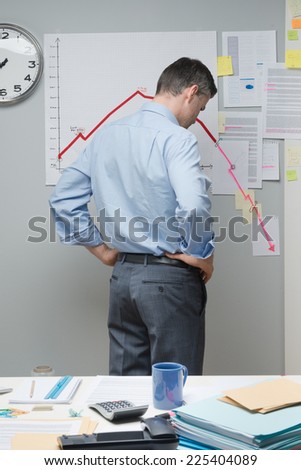 Concerned businessman at work looking at negative business chart with arrow going downwards.