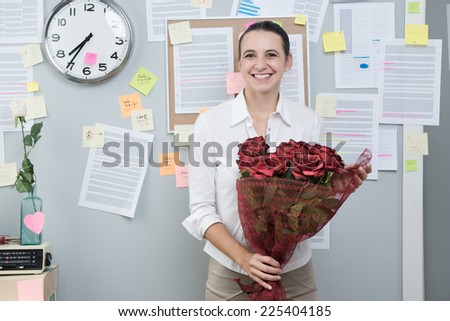 Smiling businesswoman in office standing with red roses bouquet.