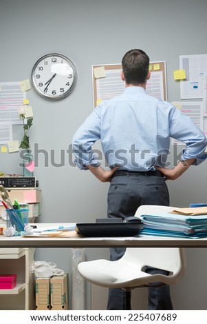 Office worker standing at workplace looking at notes on pin board.